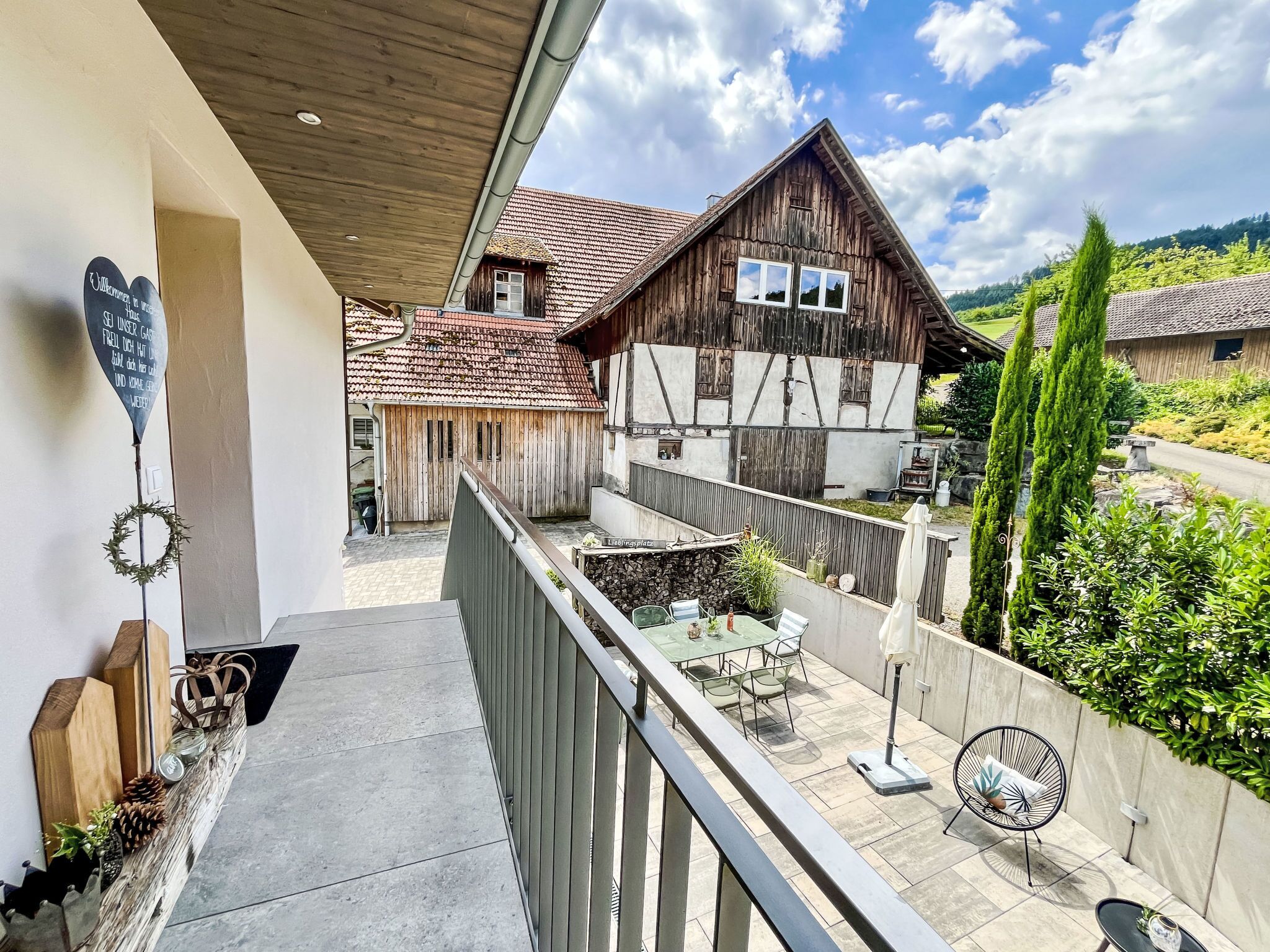 Un balcon donnant sur une maison traditionnelle en bois, un mur de pierre et un jardin.