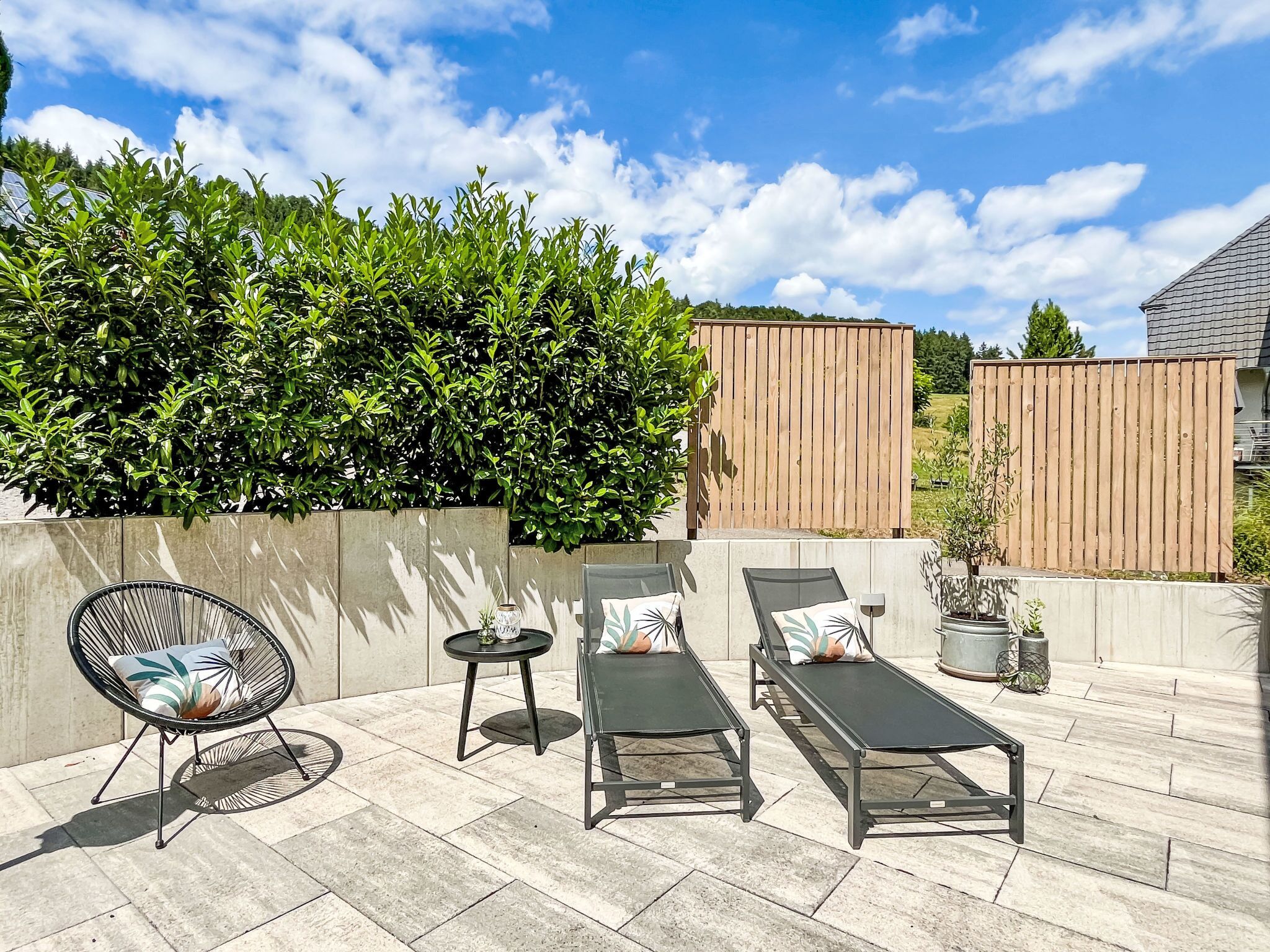 Une terrasse avec trois chaises longues, une petite table et une plante en pot.