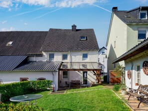 A residential area with a house featuring a sloped roof, a covered patio, and a small garden with a table and chairs. - Vacation home Bruni by Interhome (Manderscheid)