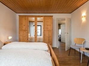 A bedroom with a wooden ceiling, a bed with white linens, a wooden wardrobe, and a chair with a wooden backrest. - Vacation home Bruni by Interhome (Manderscheid)