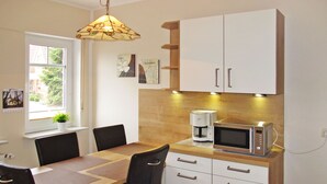 A compact kitchen with a wooden table, black chairs, a coffee maker, a microwave, and white cabinets. - Kleine Möwe by Interhome (Timmel)