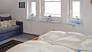 A bedroom with a large bed, a sofa, and three windows with decorative items. - Kleine Möwe by Interhome (Timmel)