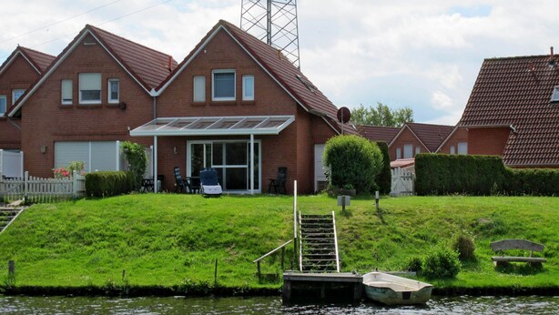 A residential house with a patio, a small boat docked by the water, and a grassy area with a bench. - Kleine Möwe by Interhome (Timmel)
