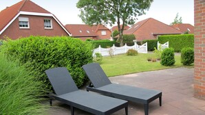 Twee comfortstoelen op een terras met een bakstenen muur en een haag op de achtergrond.