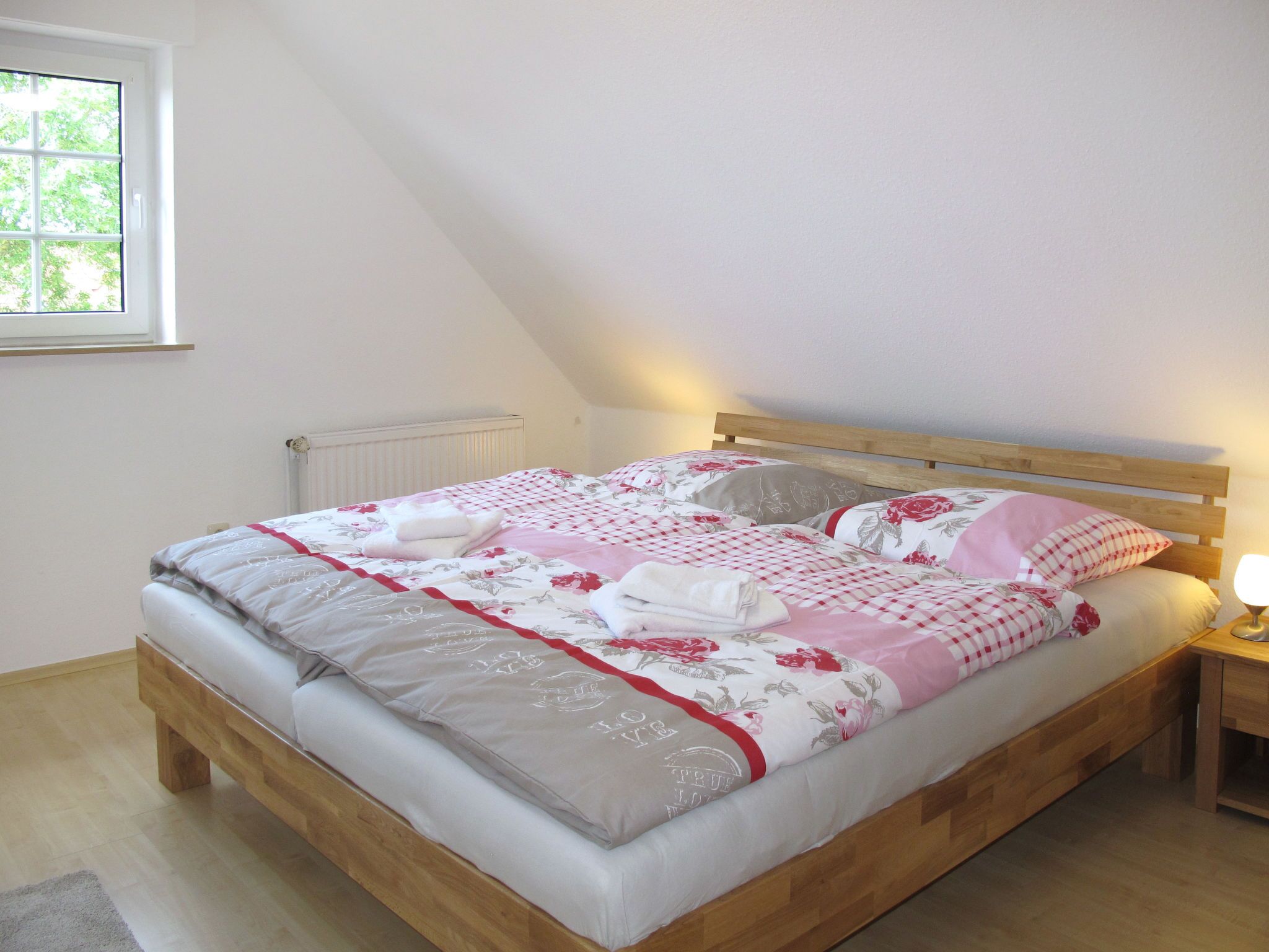 A neatly made bed with floral bedding, a wooden headboard, and a bedside table with a lamp.