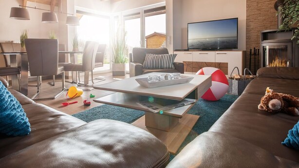 A modern living room with a wooden ceiling, a flat-screen TV, a fireplace, and a dining area with chairs and a table.