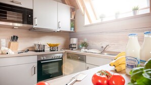 A modern kitchen with white cabinets, stainless steel appliances, and a wooden countertop. There are tomatoes, bananas, and a bottle of milk on the counter.