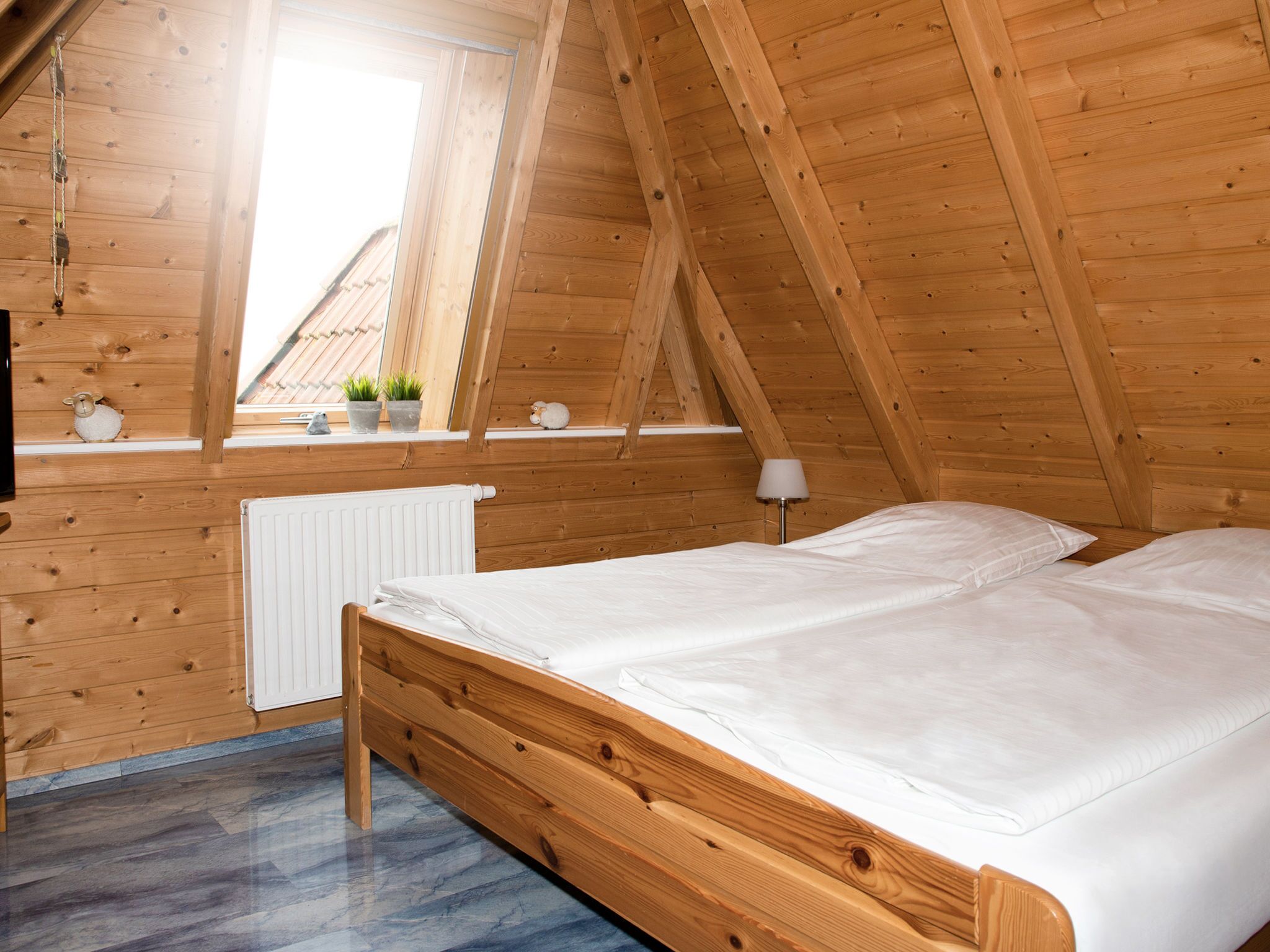 Une pièce aux murs lambrissés, avec un lit, une fenêtre et un radiateur.