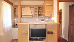 Een compacte keuken met houten kastjes, een ingebouwde televisie en een klein eetgedeelte met een stoel.