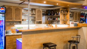 A bar area with wooden cabinets, shelves with glassware, a refrigerator with beverages, and two stools. - Vacation home Jirka by Interhome (Dehtáře)