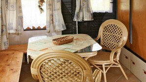 A dining area with wicker chairs and a table, a wooden bench, and a kitchen area with a clock and shelves. - Vacation home Jiri by Interhome (Dehtáře)