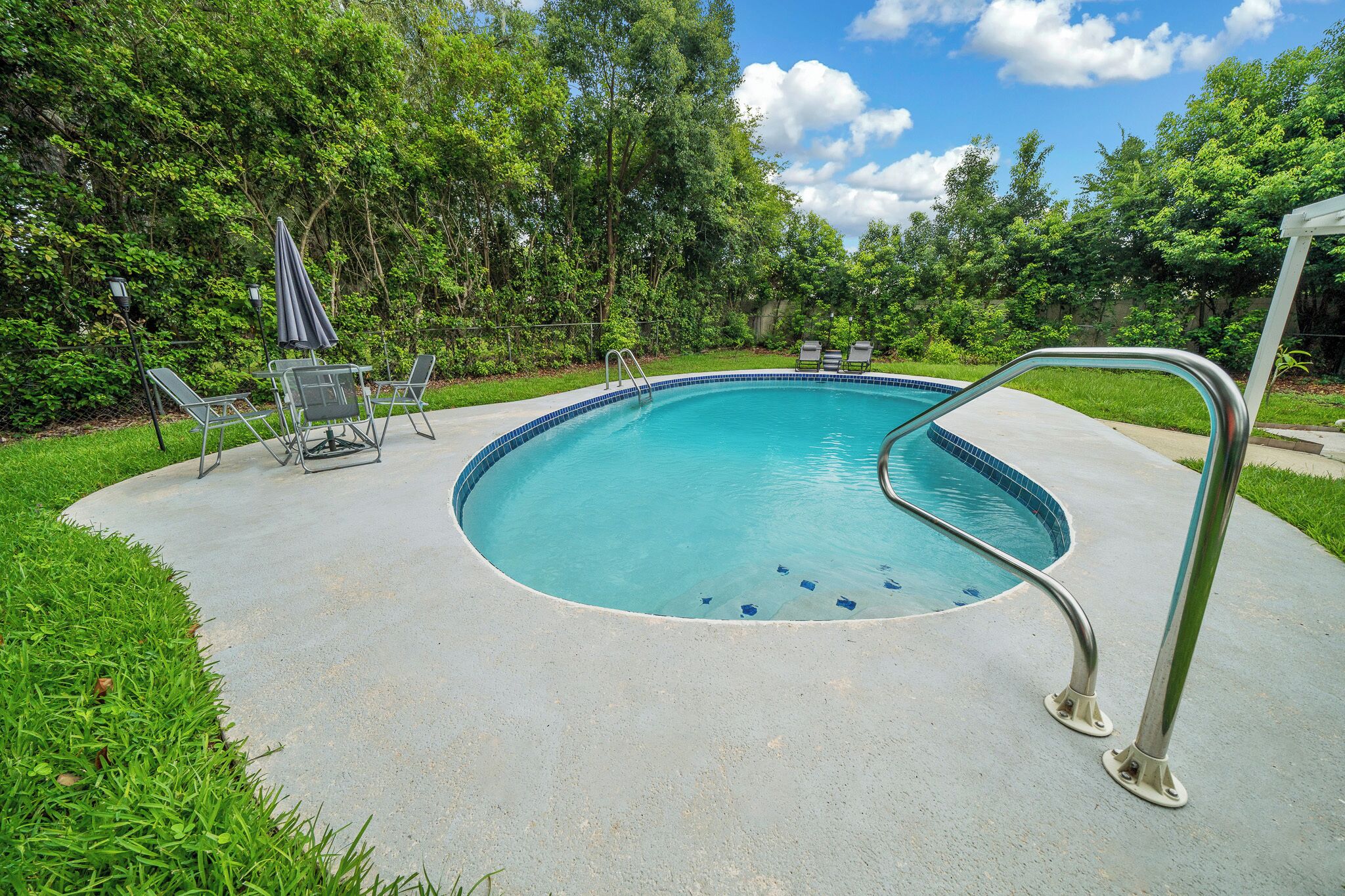 Una piscina con una escalera metálica, rodeada de césped y árboles.
