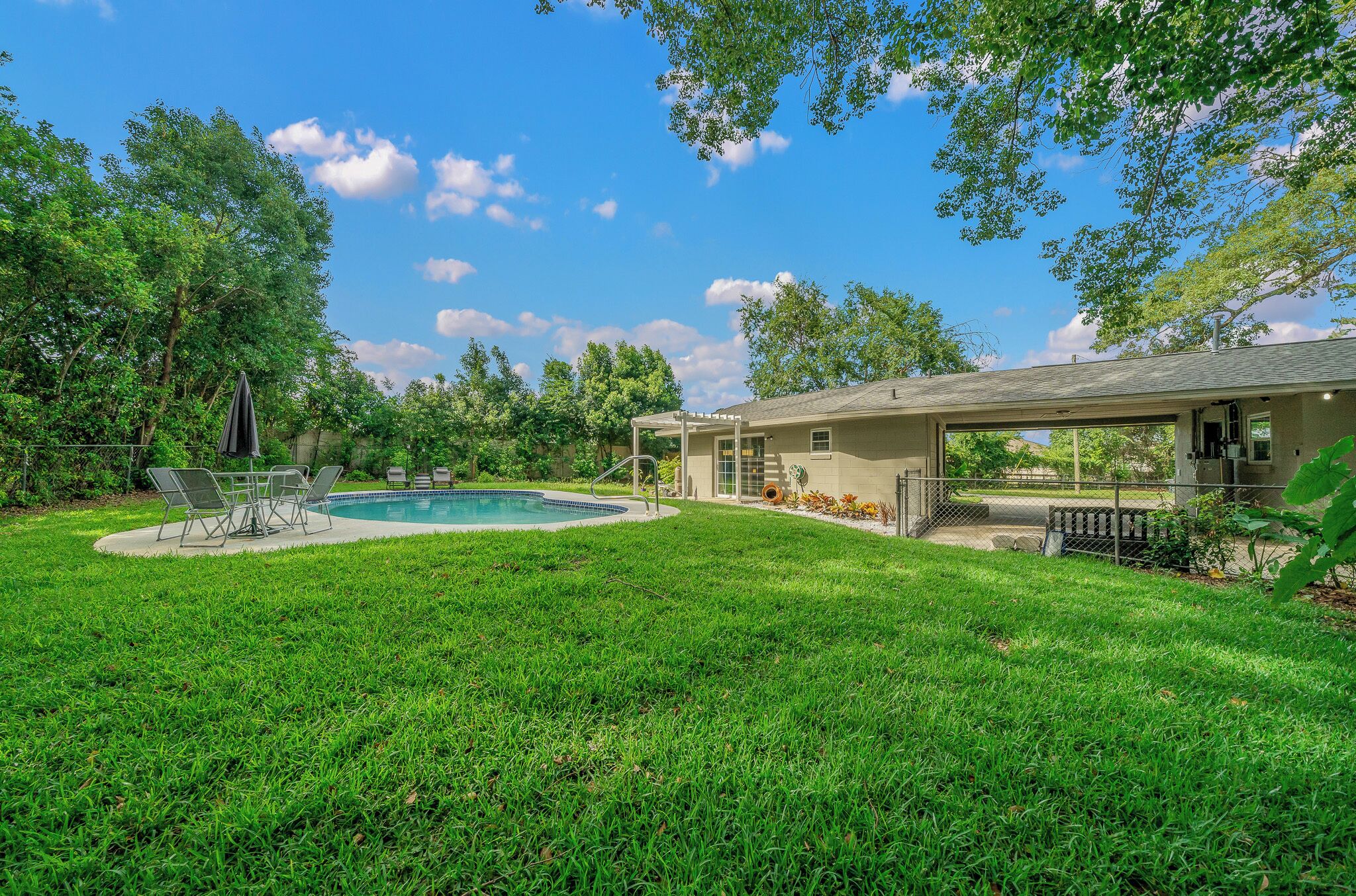 A backyard with a swimming pool, a covered patio, and a house.