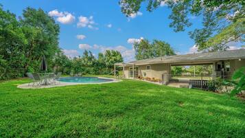A backyard with a swimming pool, a covered patio, and a house.