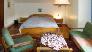 Un dormitorio con cama de madera, sillones verdes, una mesita y una lámpara colgante.