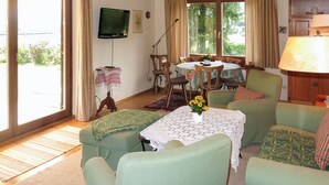 Una sala de estar acogedora con comedor, ventanas grandes, televisor y lámpara.