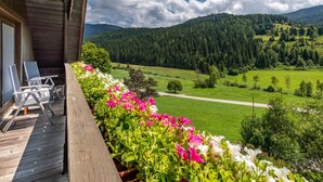 A wooden deck with outdoor seating and a view of a green valley and forested hills. - Ferienglück by Interhome (Arriach)