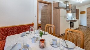 A dining area with a table set for four, a kitchen in the background, and a wooden ceiling. - Ferienglück by Interhome (Arriach)