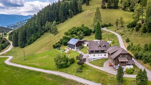 A rural house with a solar panel, surrounded by a forested hillside and a winding road. - Ferienglück by Interhome (Arriach)