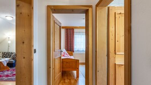 Un étroit couloir en bois mène à une chambre à coucher où se trouvent un lit en bois, une fenêtre avec des rideaux et un radiateur.