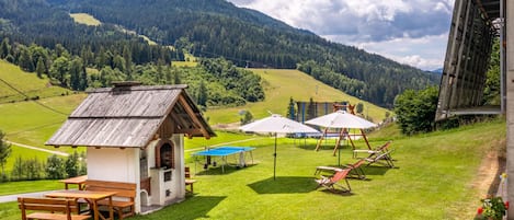 A rustic chalet with a wooden table and benches, outdoor umbrellas, and a scenic mountain view.