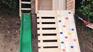 A wooden play structure with a slide and climbing wall, surrounded by trees. - The Green Studio by Interhome (Stein an der Enns)