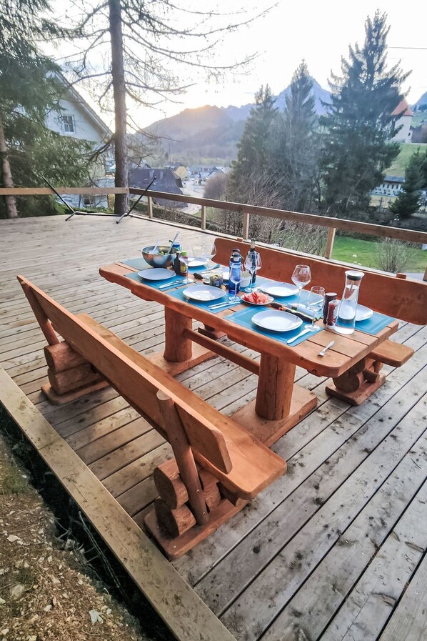 A wooden deck with a picnic table set for four, surrounded by trees and a mountain view.