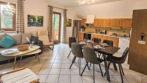 Een moderne keuken met houten kastjes, een eethoek met een tafel gedekt voor vier personen, en een zithoek met een bank en een raam.