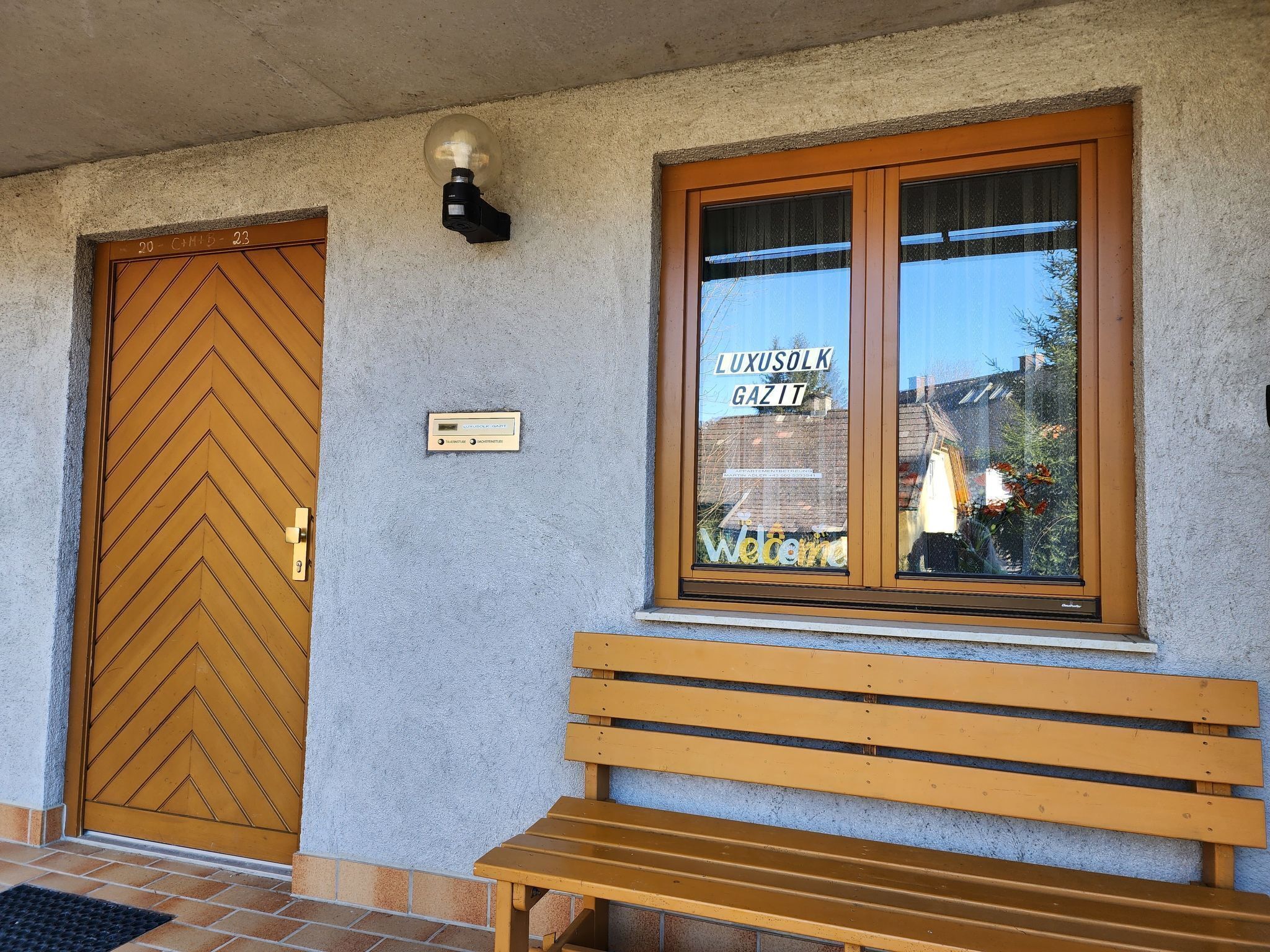 Une entrée d’immeuble avec une porte en bois, un banc et une fenêtre sur laquelle est apposée une enseigne.