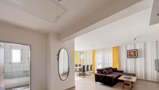 A modern living room with a sofa, a coffee table, and a dining area with chairs and a table.