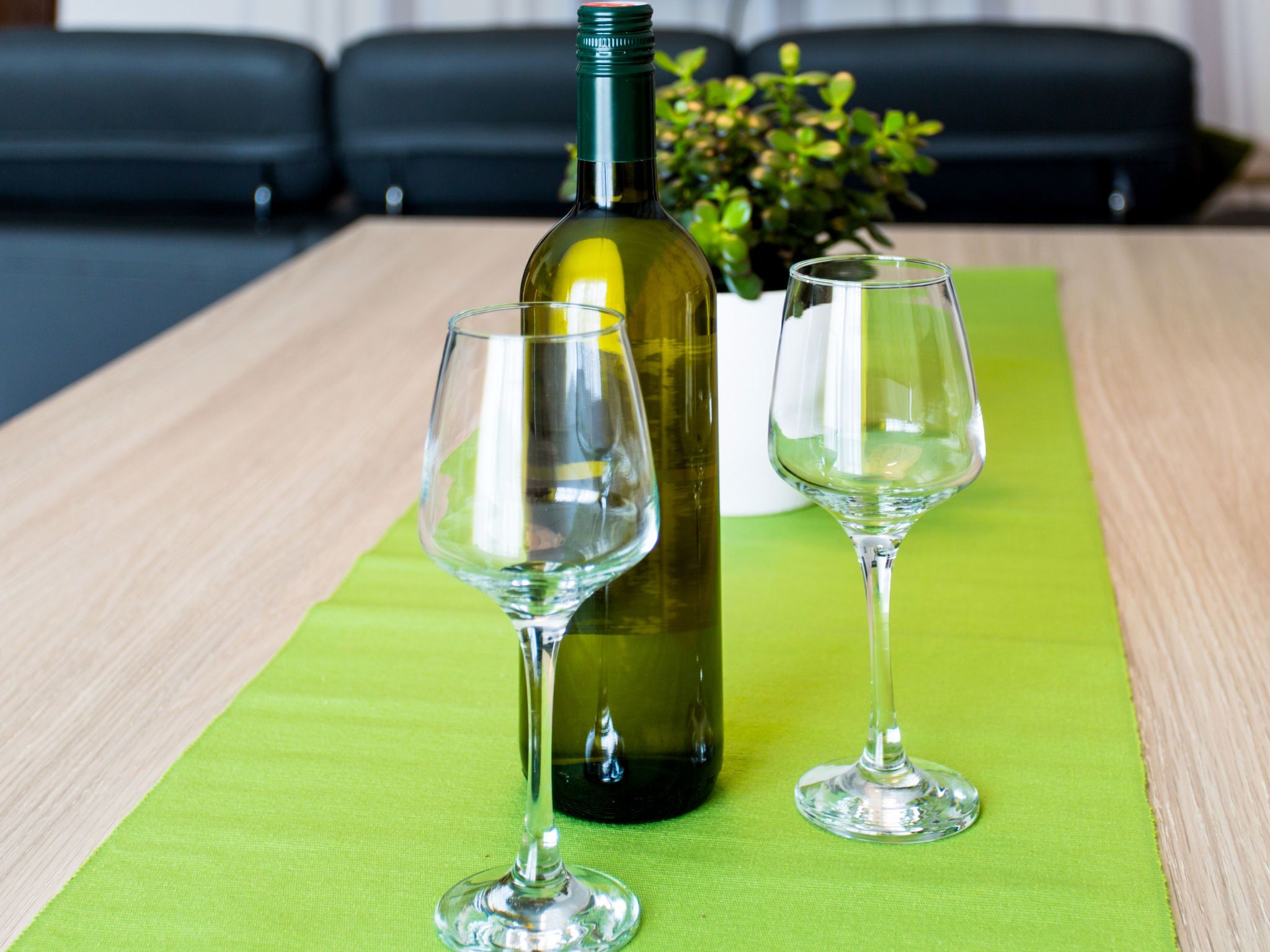 Una botella de vino y dos copas sobre un mantel verde en una habitación con asientos de cuero negro.