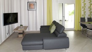 Un soggiorno moderno con un divano angolare grigio, una TV a schermo piatto, un tavolino con una pianta e un'area pranzo con tavolo e sedie.