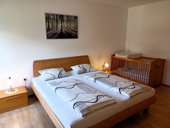 Une chambre à coucher avec une tête de lit en bois, un berceau, une lampe de chevet et un tableau représentant une forêt.