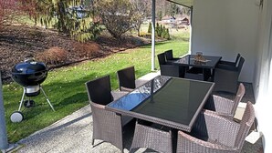 Eine Außenpatio mit Tisch, Stühlen, einem Grill und Blick auf einen Garten und Häuser.