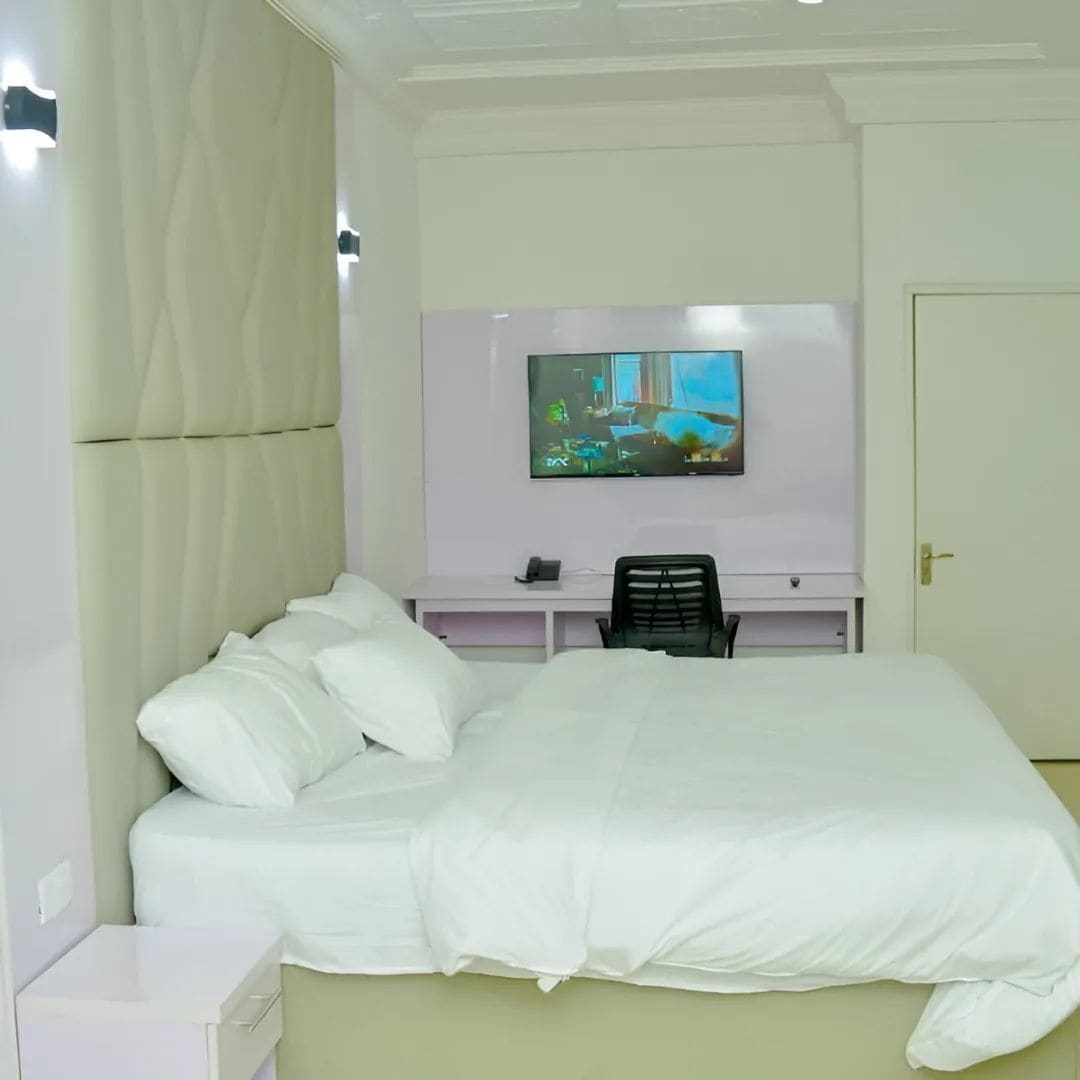Une chambre d’hôtel avec un grand lit, un téléviseur à écran plat fixé au mur, un bureau avec une chaise et une porte.