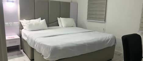 Ein Schlafzimmer mit einem Bett, einem Nachttisch, einer Klimaanlage, einem Fenster mit Jalousien und einem Sessel.