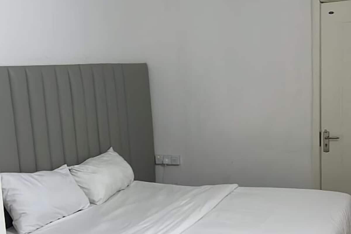 A bedroom with a bed, a grey headboard, a white door, and a patterned ceiling.