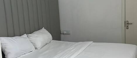 A bedroom with a bed, a grey headboard, a white door, and a patterned ceiling.