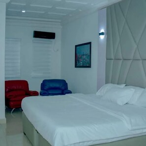 Een slaapkamer met een bed, een rode stoel, een blauwe stoel en een schilderij aan de muur.