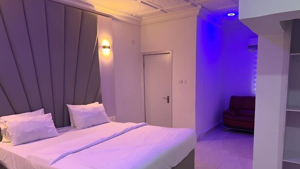 Une chambre moderne avec un grand lit, une porte et un coin salon avec un fauteuil rouge.