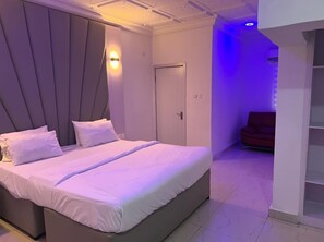 A modern bedroom with a large bed, a door, and a seating area with a red chair. - Mansion Signature Homes (Benin City)