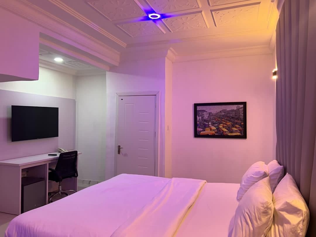 A hotel room with a bed, a desk, a chair, a television, and a door.