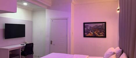 A hotel room with a bed, a desk, a chair, a television, and a door.