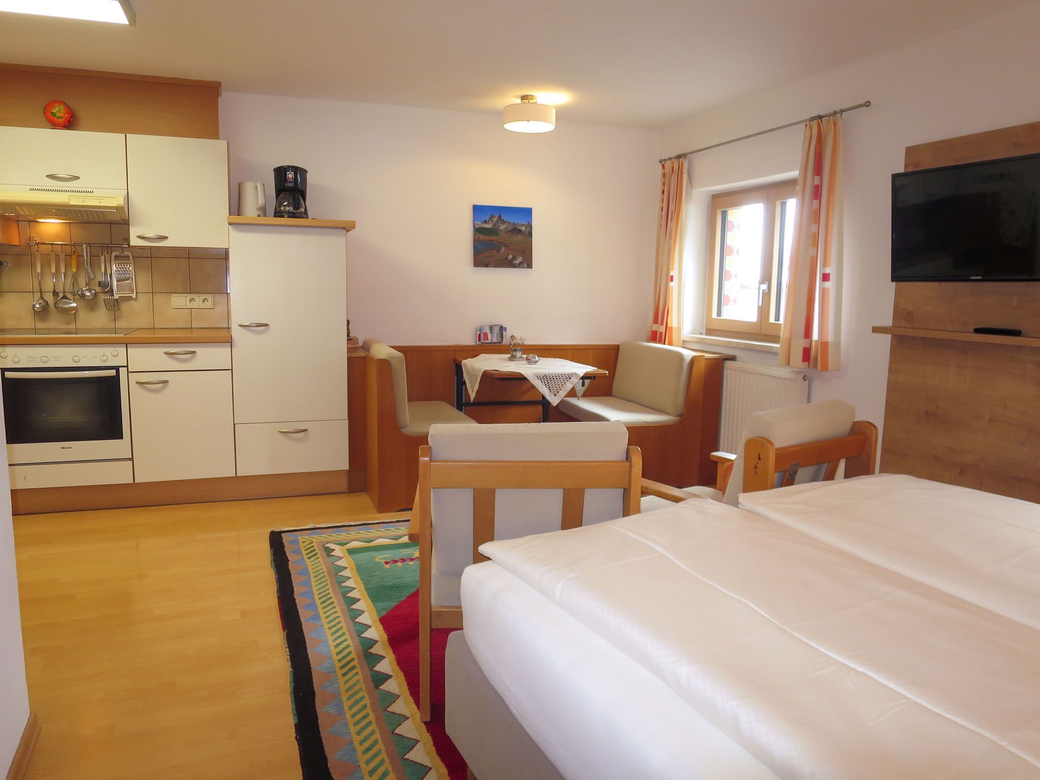 A compact hotel room with a kitchenette, a bed, a small dining table, and a TV.