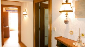 Un couloir avec une porte en bois, une lampe fixée au mur et une petite table sur laquelle se trouve une bougie.