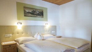 Un lit double avec du linge de lit blanc, une table de chevet en bois avec une lampe, et un tableau encadré au mur.
