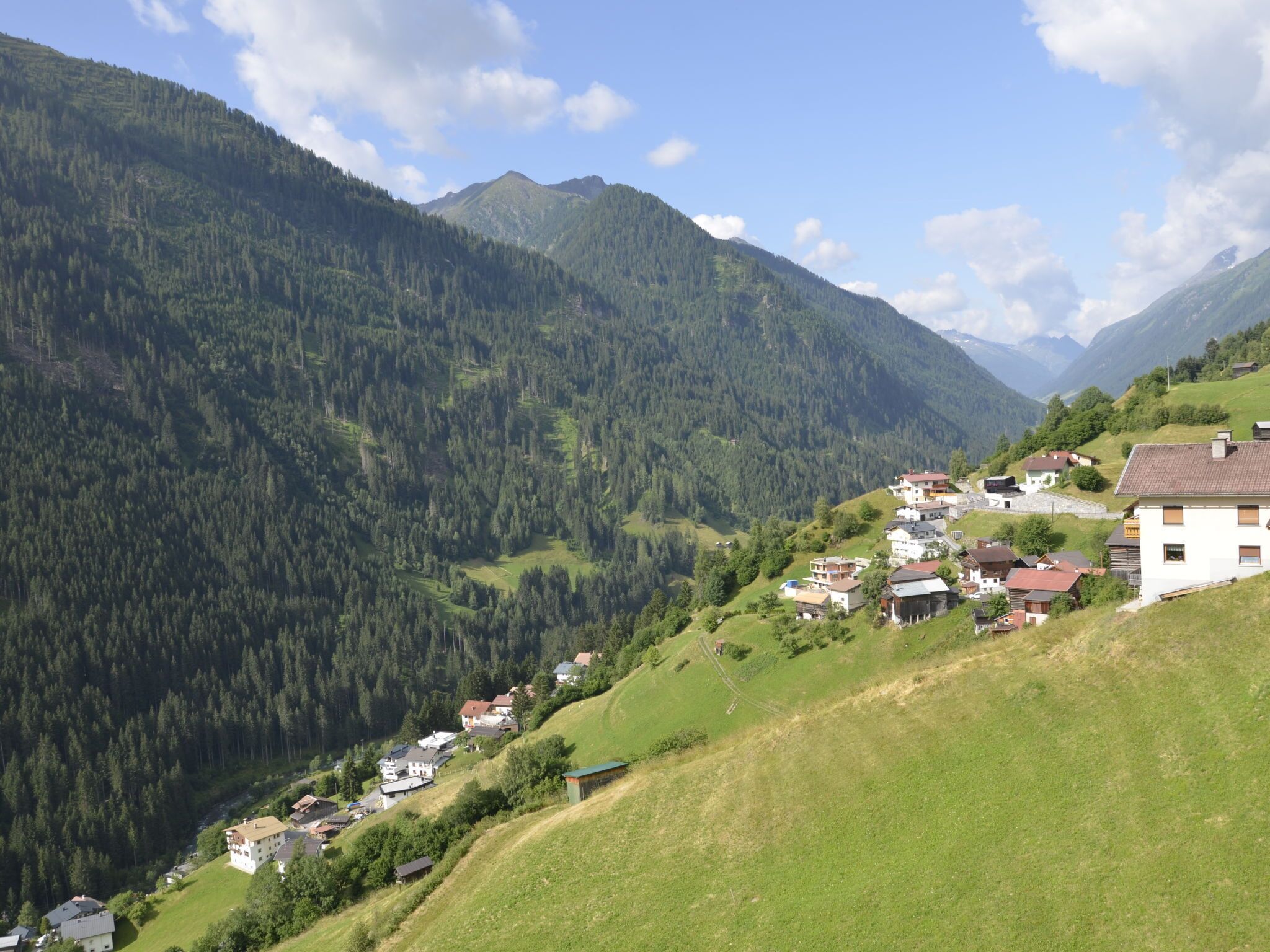 A mountainous village with houses on a hillside, surrounded by dense forest and mountains.