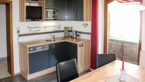 A compact kitchen with a microwave, stove, and sink. There is a dining table with chairs and a candle.