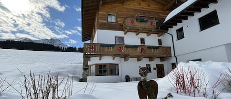 Un chalet en bois à deux étages, doté d’un balcon orné de rubans rouges, et entouré de neige.