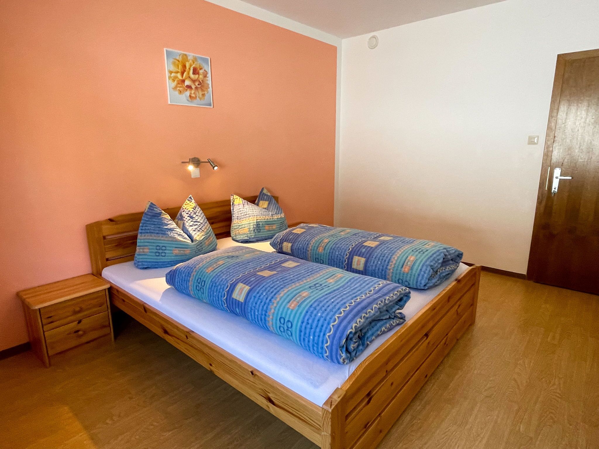 Ein Zimmer mit einem Einzelbett, einem hölzernen Bettgestell, einem kleinen Nachttisch und einem Beistelltisch.